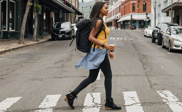 Woman crossing the street while carrying an iced coffee drink and wearing the Shadow Guide 33.